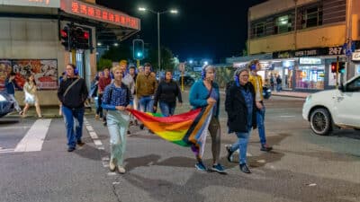 A group of people with headphones holding a pride flag walking on a busy street.