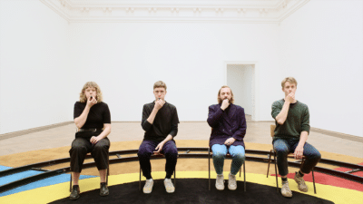 Four people seated, blowing whistles